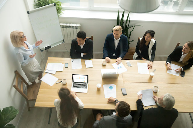 Aged senior businesswoman giving presentation at multiracial group office meeting